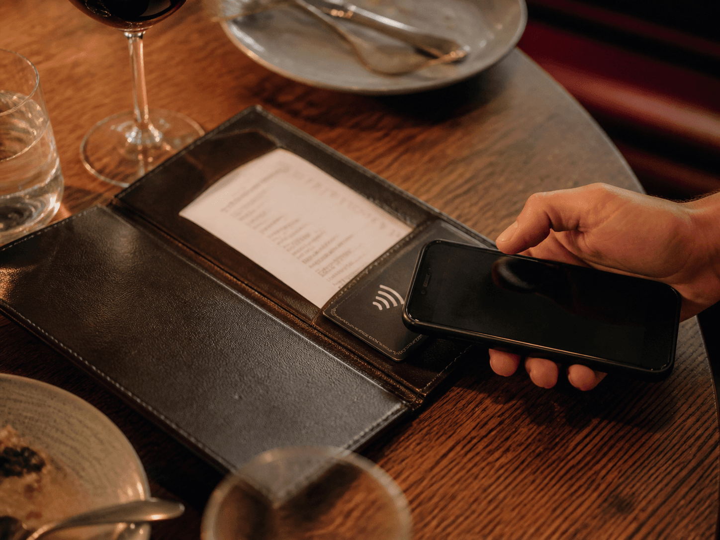 A diner tapping their phone on an NFC review card in a restaurant bill folder